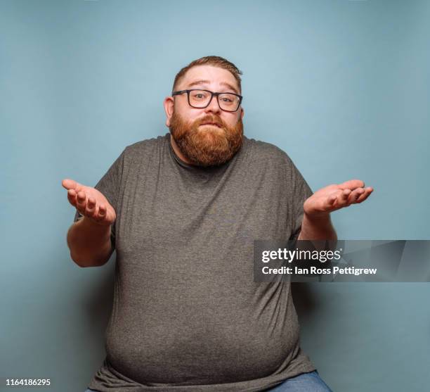 overweight bearded hipster on blue background - shrugging stock-fotos und bilder