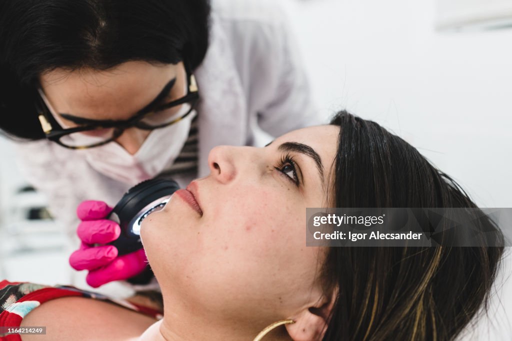 Examen de la piel del paciente con una lente dermatológica