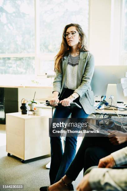 Portrait of businesswoman holding laptop and listening to coworkers during informal meeting in office