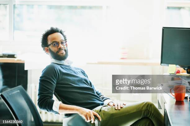 portrait of businessman seated at workstation in office - green pants stock-fotos und bilder