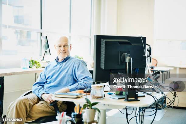 Portrait of senior male business owner seated at computer workstation in start up office
