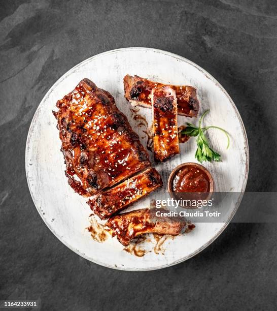 full rack of grilled barbecue ribs with barbecue sauce on cutting board on black background - rippchen stock-fotos und bilder