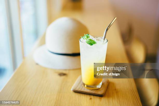 a glass of refreshing iced passion fruit and mango soda served on table in the cafe, next to a straw hat in a hot summer day - mango juice stock pictures, royalty-free photos & images