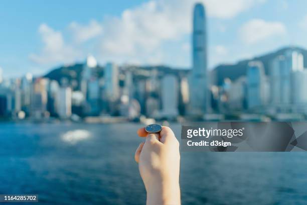 close up of human hand holding coin and getting ready to flip against hong kong cityscape and victoria harbour on a sunny day - coin toss stockfoto's en -beelden