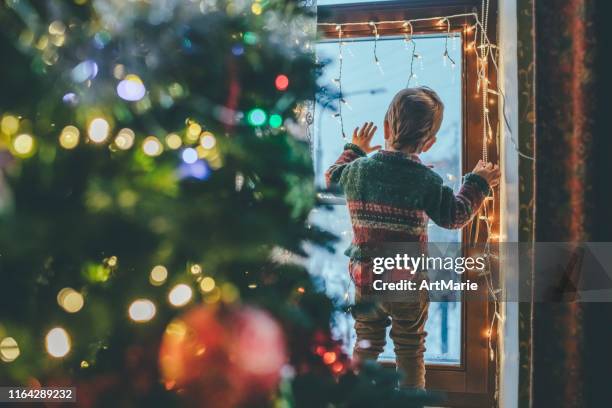 bambino che gioca con le luci di natale a casa - guardare fuori dalla finestra foto e immagini stock
