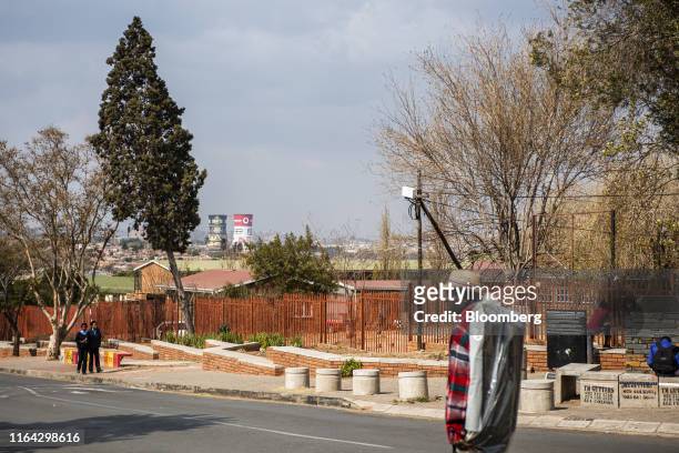 Pedestrians walk along the street as the cooling towers of the decommissioned Orlando Power Station stand in the distance in Kliptown, Soweto, South...