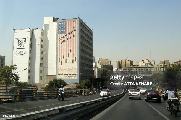 Cars drive past a mural painted on the wall of a building showing an anti US slogan in the capital Tehran on August 27, 2019. - Iranian President...