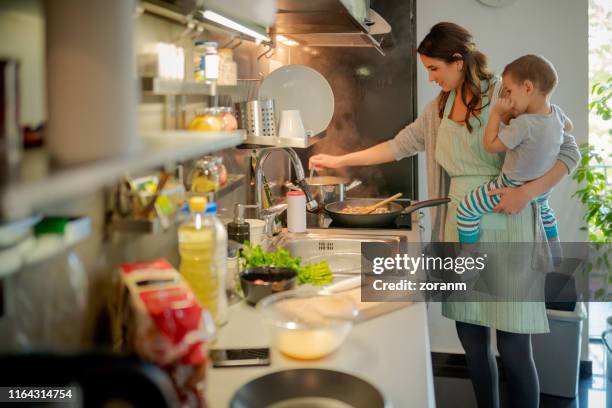 mother stirring food with the toddler on hip - stay at home mother stock pictures, royalty-free photos & images