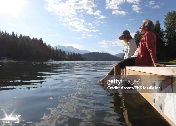 mature couple relax on a dock over a mountain lake - vorruhestand stock-fotos und bilder
