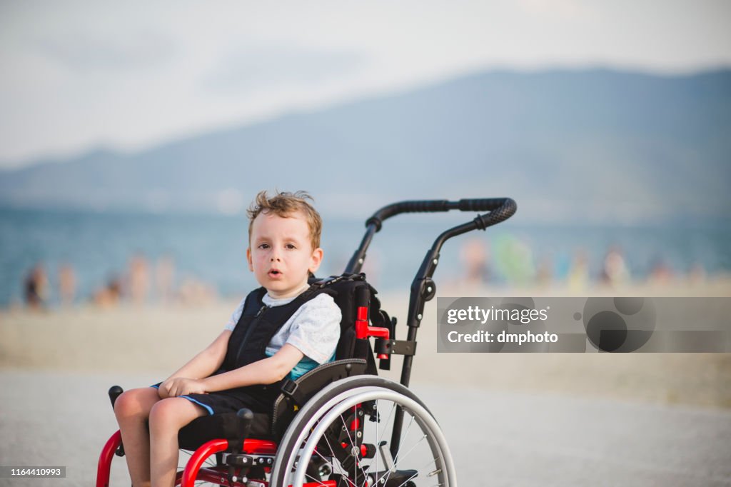 Cute young boy on the wheelchair by the sea