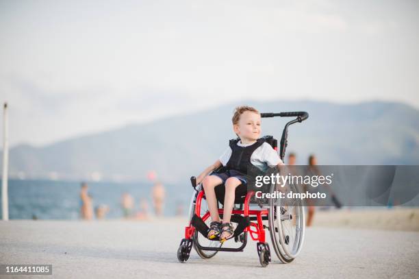 smiling young boy on the wheelchair by the sea - atrophy stock pictures, royalty-free photos & images
