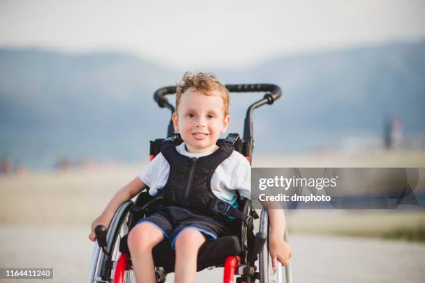 niño sonriente en la silla de ruedas junto al mar - atrofia fotografías e imágenes de stock