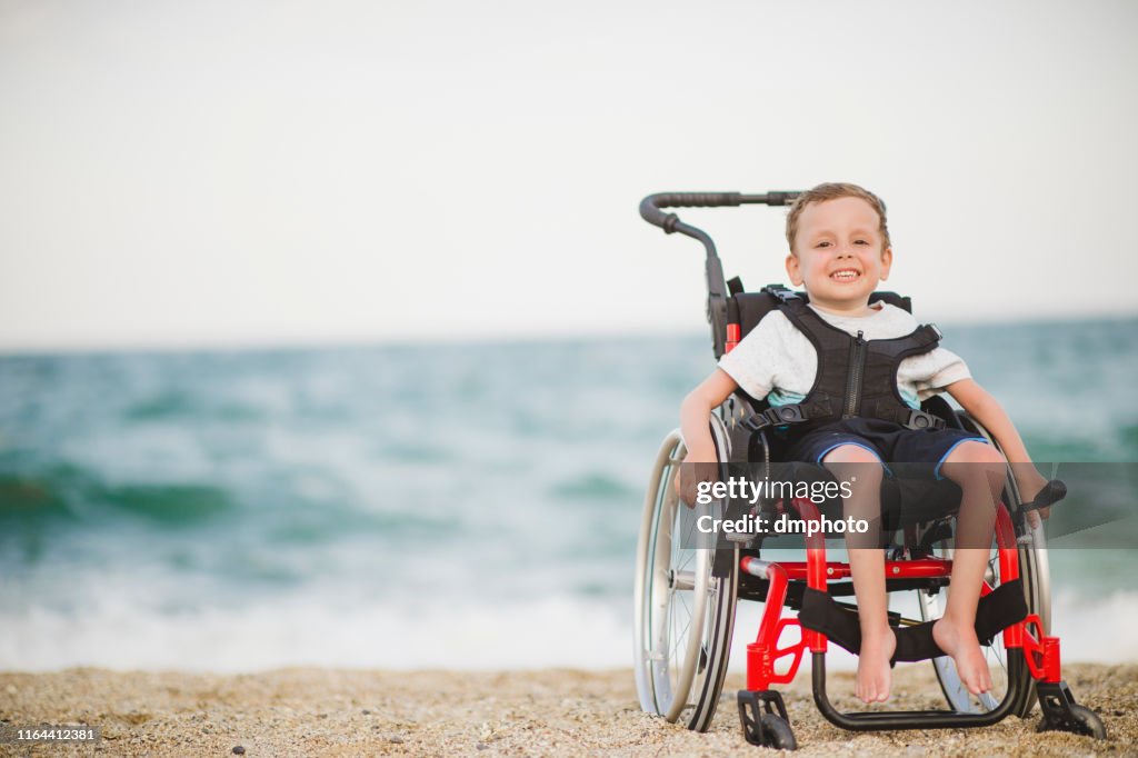 Smiling young boy on the wheelchair by the sea