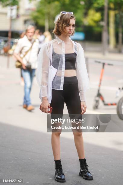 Guest wears sunglasses, a transparent white shirt, black cropped top, black short leggings, black leather shoes, during Paris Fashion Week -Haute...
