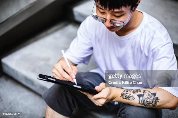young asian man using digital devices on staircase - drawing on tablet stock pictures, royalty-free photos & images