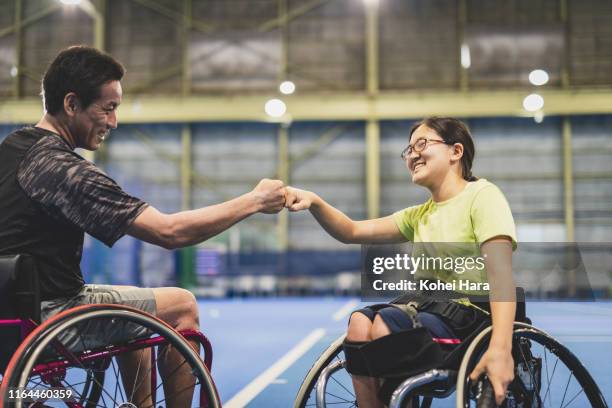 Disabled female athlete doing a fist bump with her coach during playing wheel chair tennis