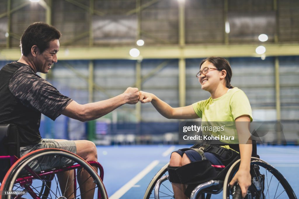 Disabled female athlete doing a fist bump with her coach during playing wheel chair tennis