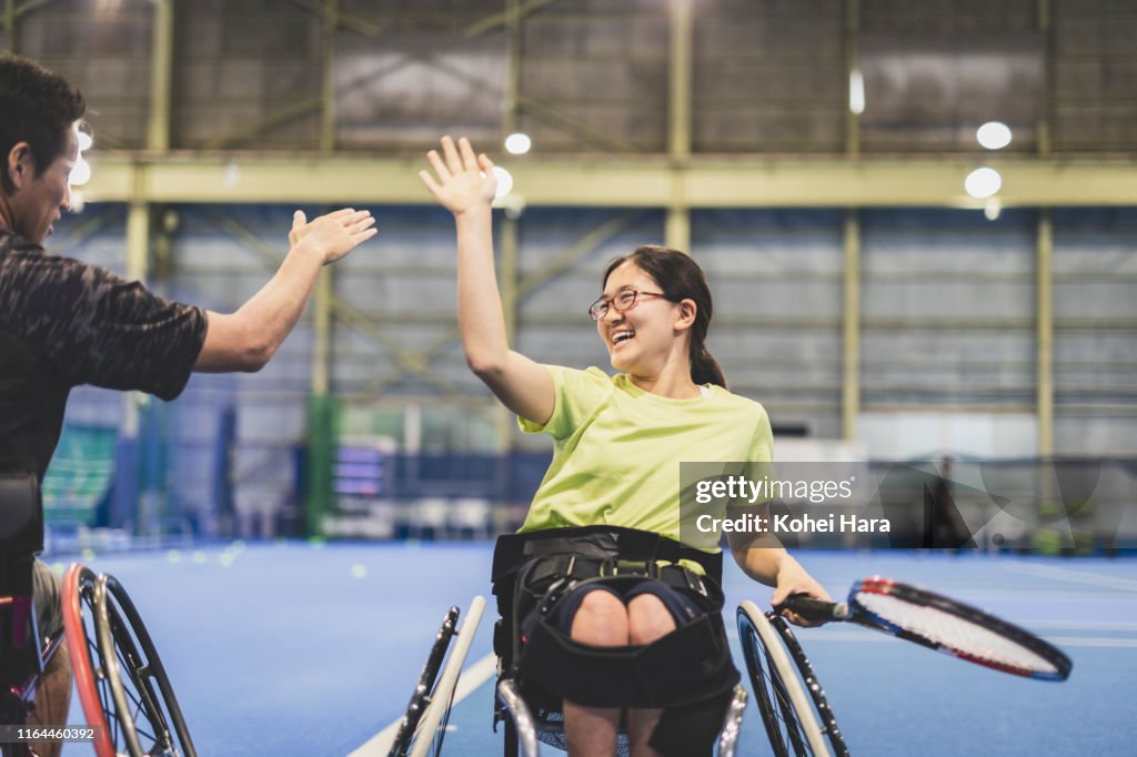 Disabled female athlete doing a high five with her coach during playing wheel chair tennis