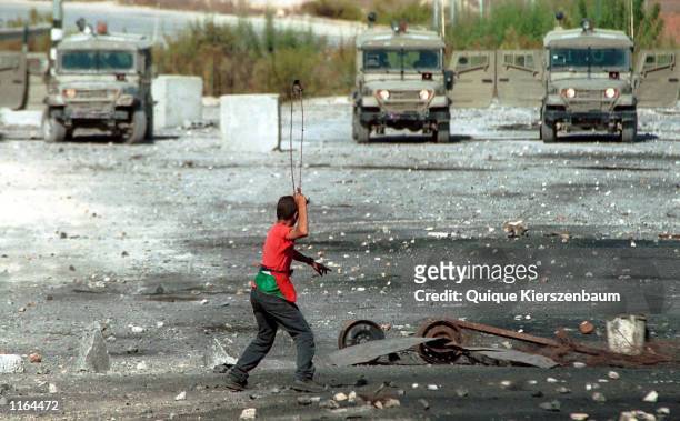Palestinian demonstrator uses a slingshot to throw stones at Israeli Army Jeeps during clashes with Israeli soldiers September 28, 2001 in the...