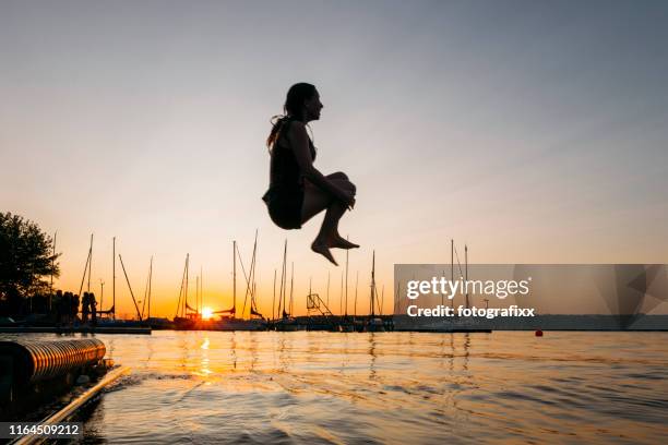 summer day: young woman jump from jetty into lake while sunset - cannonball diving stock pictures, royalty-free photos & images