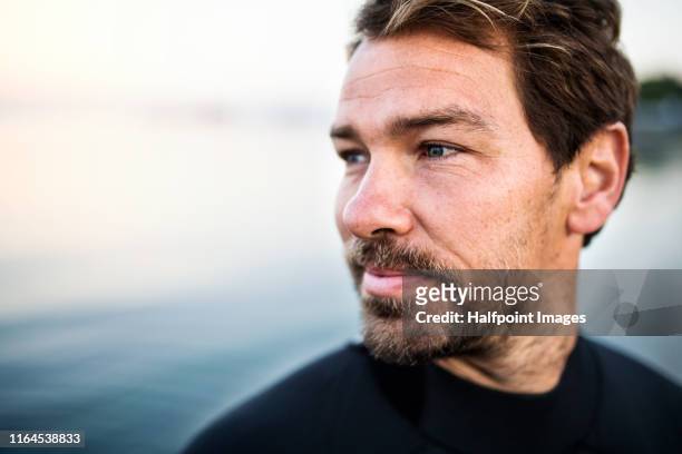 a fit mature sportsman with wetsuit standing outdoors on beach, a close-up. - determination male stock pictures, royalty-free photos & images