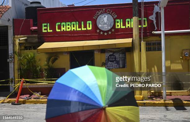 Woman with an umbrella walks past the Caballo Blanco bar on August 28, 2019 a day after at least 26 people were killed and 11 badly wounded after...