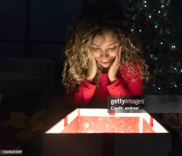 donna felice che apre un regalo di natale e sembra sorpresa - sorpresa regalo foto e immagini stock