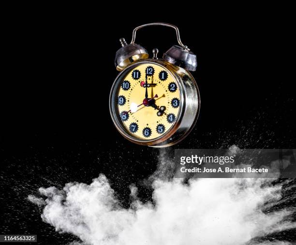 explosion by to the impact of an alarm clock of a cloud of particles of powder and smoke of color white on a black background. - blast from the past stock pictures, royalty-free photos & images