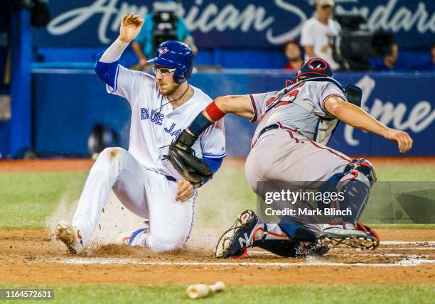 Danny Jansen of the Toronto Blue Jays is safe at home plate against Tyler Flowers of the Atlanta Braves in the sixth inning at the Rogers Centre on...