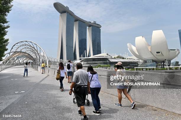 People walk across the bridge near Marina Bay Sands Skypark and the ArtScience Museum in Singapore on August 29, 2019.