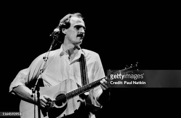 American Folk musician James Taylor plays acoustic guitar as he performs onstage at the Poplar Creek Music Theater, Hoffman Estates, Illinois, June...