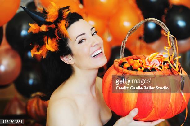 beautiful smiling brunette woman dressed up for halloween holding a basket filled with candies with black and orange balloons in the background - candy corn imagens e fotografias de stock