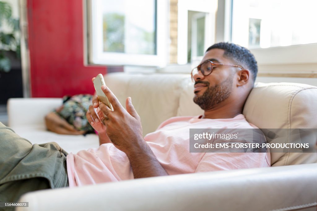 Relaxed man sitting on sofa using cell phone