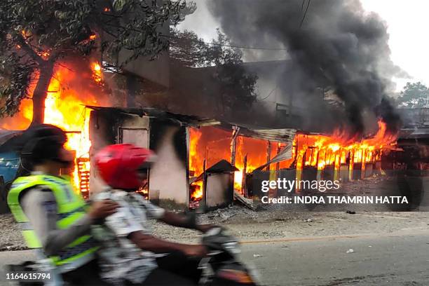 Motorist ride past a burning building after hundreds of demonstrators marched near Papua's biggest city Jayapura on August 29 where they set fire to...