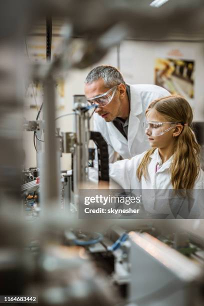 männliche laborarbeiterin lehrt kleine mädchen über maschinenteile im labor. - science lab school stock-fotos und bilder