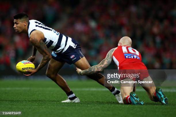 Tim Kelly of the Cats hand-passes as he is tackled by Zak Jones of the Swans during the round 19 AFL match between the Sydney Swans and the Geelong...