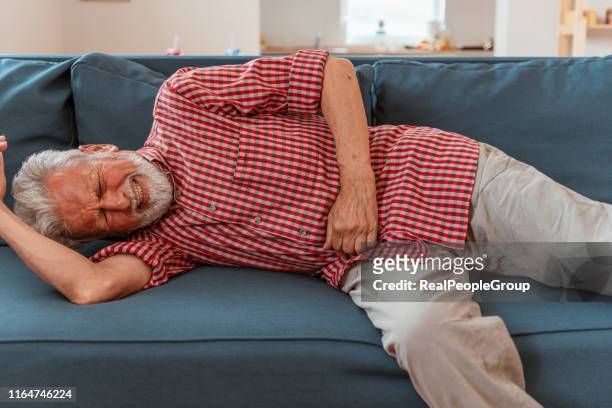 schrecklicher magenschmerz. kranker senior mann leidet unter magenschmerzen halten seinen magen im schlafzimmer - verstopfung stock-fotos und bilder
