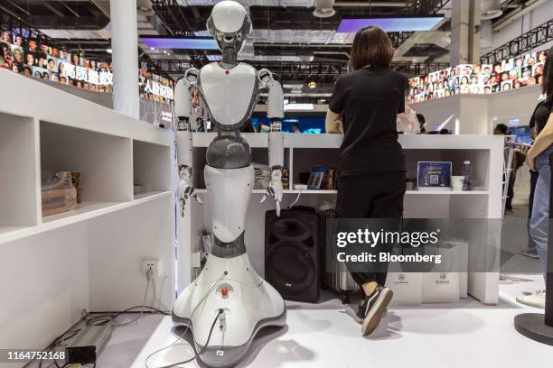 An attendant stands next to a CloudMinds Technology Inc. XR-1 commercial humanoid service robot at the World Artificial Intelligence Conference in...