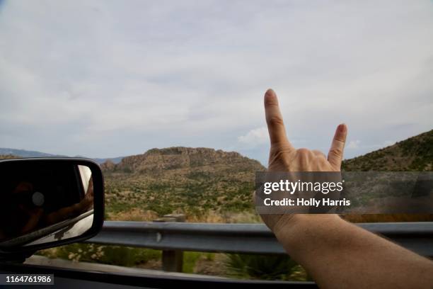 hand gesture devil horns implying "rock out", arm out window on road trip - car horn stock-fotos und bilder
