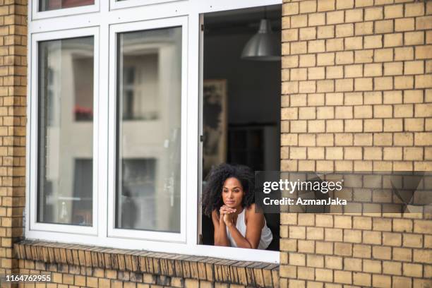 kontemplative afrikanische geschäftsfrau steht am fenster - mit ellenbogen gestützt stock-fotos und bilder