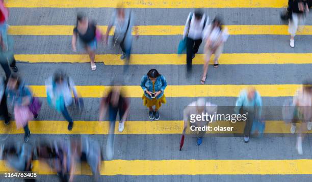 young woman standing, with phone, in motion blurred crowd - standing out from the crowd stock pictures, royalty-free photos & images
