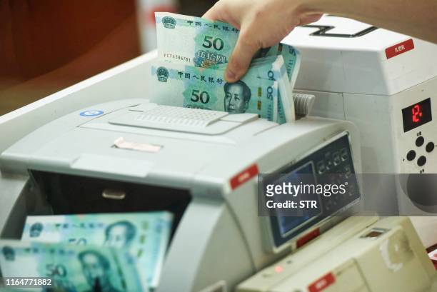Chinese bank employee counts new 50-yuan notes with a money counting machine at a bank counter in Hangzhou in China's eastern Zhejiang province on...