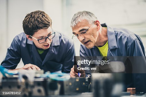 Senior engineer explaining machine functioning to his student Senior engineer explaining machine functioning to his student