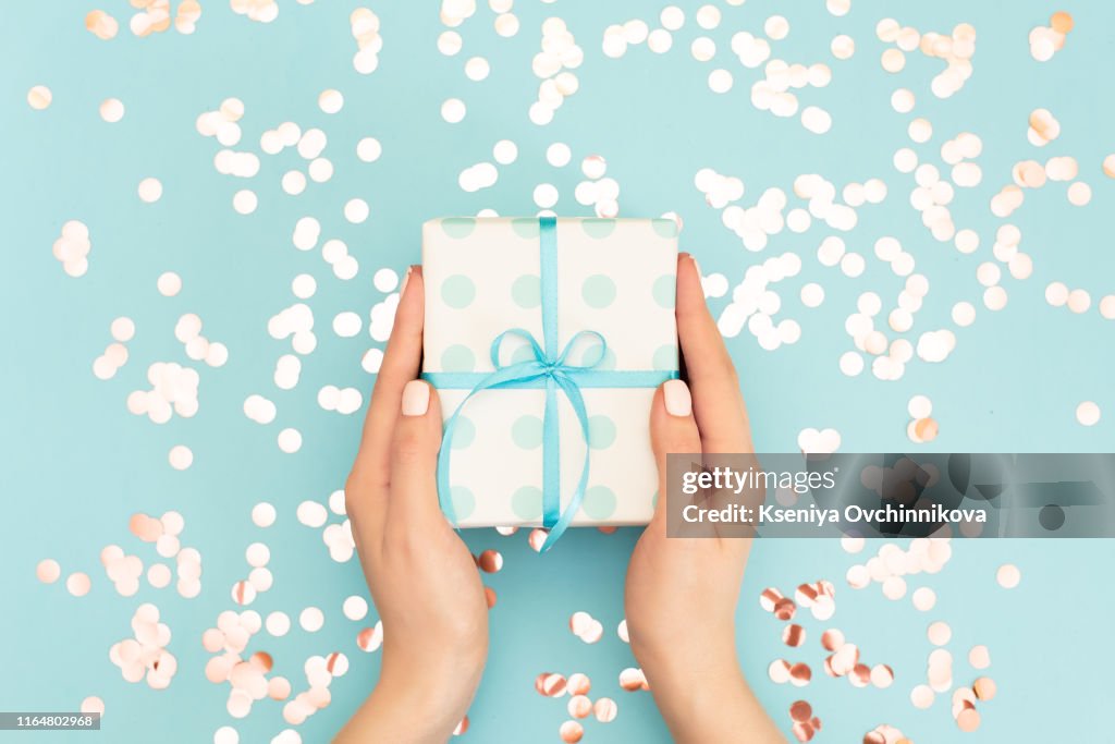 Womans hands holding gift or present box decorated confetti on pink pastel table top view. Flat lay composition for birthday or wedding.