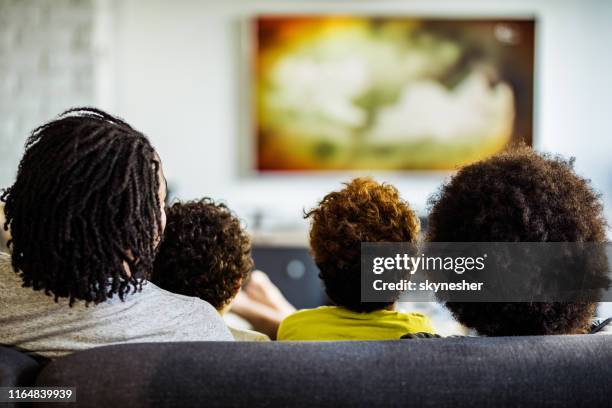 vista sul retro di una famiglia che guarda la tv nel soggiorno. - african watching tv foto e immagini stock