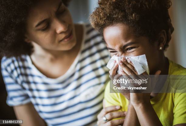 black mother consoling her daughter who is blowing a nose. - child illness stock pictures, royalty-free photos & images