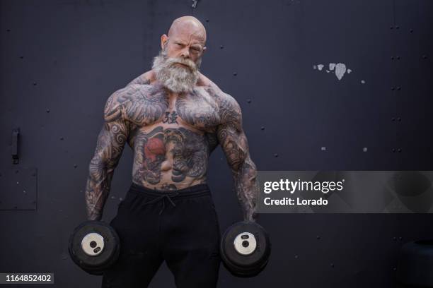 tatuado hombre senior durante el entrenamiento de gimnasio - handsome bodybuilders fotografías e imágenes de stock