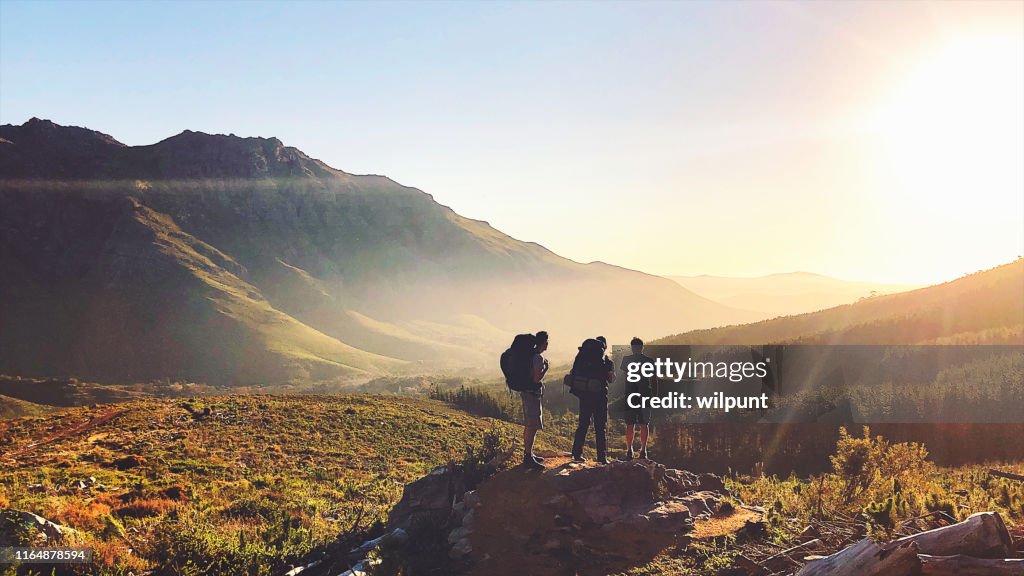 Rearview of Hikers with backpacks enjoying the sunset in the mountains