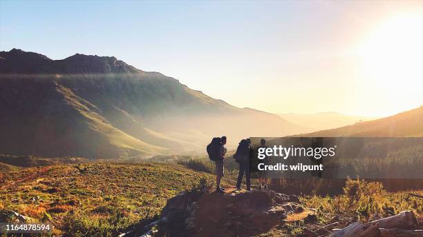 rearview av vandrare med ryggsäckar njuter av solnedgången i bergen - three people bildbanksfoton och bilder