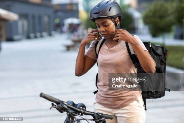 donna delle consegne africana che regola il casco da ciclismo - postino foto e immagini stock